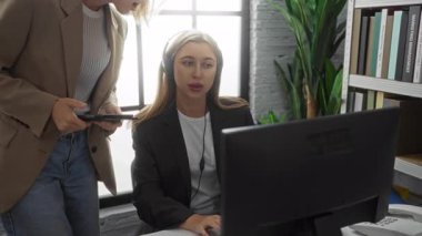 Modern bir ofiste çalışan kadınlar, biri kulaklık, diğeri ise kitap ve bitkilerle çevrili bir tablet kullanıyor ve profesyonel bir çalışma ortamı yaratıyorlar..