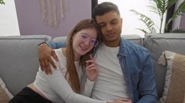 Çift rahat bir oturma odasında rahat bir kanepede gülüyor ve sarılıyor, evde sevgi ve rahatlık sergiliyor, sıcak ve samimi bir atmosfer yaratıyor..