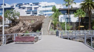 Lanzarote, İspanya 'daki bir açık hava sahnesinin bulanık görüntüsü, bir sahil kenarında bir bank, konut binaları, yemyeşil yemyeşil ve kanarya adalarında açık mavi bir gökyüzü..