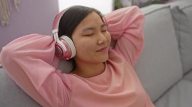 Oturma odasında rahat bir kulaklık takan kadın sakin bir ifadeyle müziğin tadını çıkarıyor..