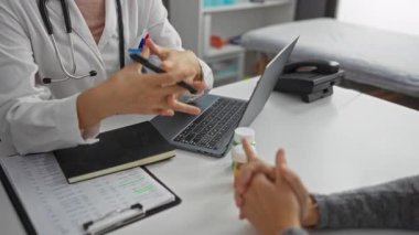 Kadın doktor klinikteki hastalarla konuşuyor, sağlık hizmetleri, dizüstü bilgisayar, steteskop, not defteri ve ilaç şişesini masaya koyuyor..