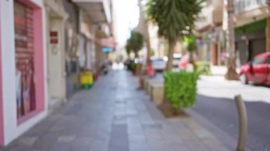Ağaçlarla, park edilmiş arabalarla, dükkanlarla ve güneşli bir günde yürüyenlerle bulanık şehir caddesi.