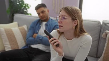 Oturma odasında kadın ve erkek, bir kanepede oturuyorlar, sohbet ediyorlar, ilişki dinamiklerini gösteriyorlar, modern bir ev içinde..