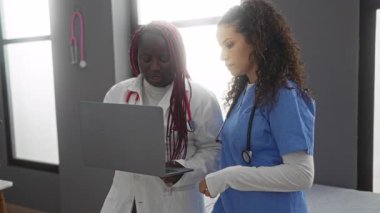 Klinik bir ortamda çalışan iki kadın sağlık uzmanı hastanede dizüstü bilgisayar kullanarak hasta bilgilerini tartışıyorlar..