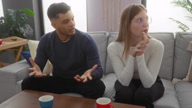 Çift, evdeki kanepede kadın jestleri ve modern bir oturma odasında erkek özentisi ile tartışıyor..