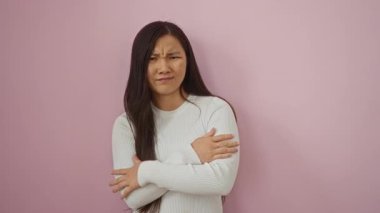 Pembe arka plana karşı jestlerle onaylamadığını ifade eden bir kadın, açık renk bir kazak giyen genç, Asyalı, yetişkin bir kadın.