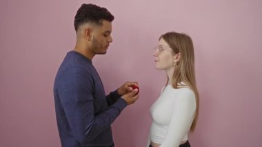 Bir erkeğin pembe arka planda yüzüğü olan bir kadına evlenme teklif etmesi, bir çiftin ilişkilerinde reddedilme ve duygu anlarını resmediyor..