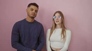 Kadın ve erkek, parmakları dudaklarının üzerinde sessiz bir şekilde pembe bir arka plana yaslanarak neşeli ve sevgi dolu bir çiftin dinamiklerini sergiliyorlar..