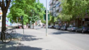 Bulanık şehir caddesi. Arabalar yan yana park edilmiş. Ağaçlar güneşli bir günde kaldırıma dizilmiş.