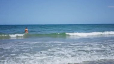 Bulanık dalgalar ve güneşli bir günde arka planda gökyüzü ile okyanusta yüzen odaksız bir adam.