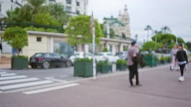 İnsanlar Monako 'da lüks bir caddede geziyorlar. Zarif binaların ve egzotik yeşilliklerin bulanık geçmişleri var..