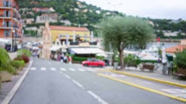 Bokeh manzaralı Villlefranche-sur-mer caddesi. Bulanık binalar, insanlar ve arabalar gün boyunca Fransız kasabasında yemyeşil alanlarla çevrili..