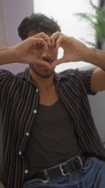 Sakallı genç adam, elleri ile kalp oluşturan şık bir oturma odasında otururken rahat ve rahat bir atmosfer yaratıyor..