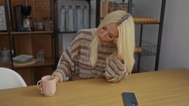 İçerde, rahat bir oturma odasında kahvesini yudumlayan bir kadın, süveter giyen çekici bir sarışın, bir apartman dairesinde oturan bir yetişkin..