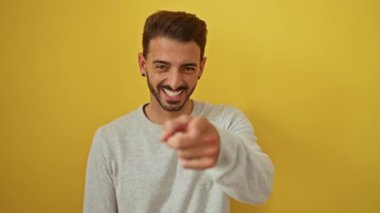 Genç adam, neşeli, izole edilmiş bir portreye güven ve neşe saçan, canlı sarı bir arka plana kamerayla bakarken gülüyor..