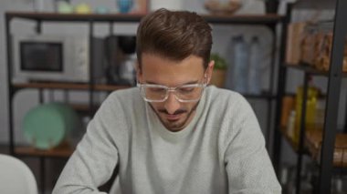 Raflar ve mutfak aletleriyle çevrili modern bir ofiste gülümseyen gözlüklü genç adam, profesyonel ortamlar için rahat ve ulaşılabilir bir atmosfer yaratıyor..