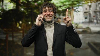 Bir şehir caddesinde açık havada yetişmiş, telefonda konuşurken gülümseyen genç İspanyol adam kendine güvenen ve çekici bir kişilik sergiliyor..