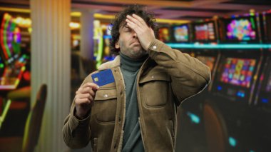 Kumarhanede gergin bir anı yansıtan canlı kumarhane kumar makinelerinin yanında kredi kartı tutan bir adam evde hayal kırıklığı yaşıyor..