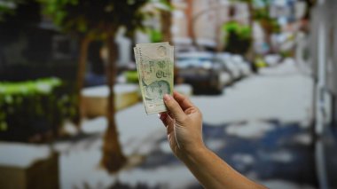 Güneşli bir şehir caddesinde el ele tutuşan banknotlar, canlı bir şehir ortamında uluslararası finans ve döviz alışverişini sembolize ediyor..