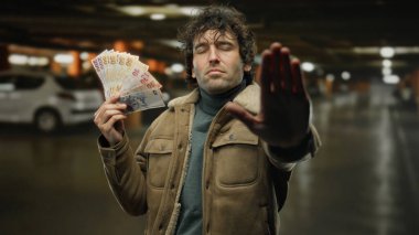 Kapalı alanda elinde Türk banknotları tutan İspanyol bir adam bir park alanında durup, kapalı bir alanda para, finans ve kişisel sınır vurguluyor.