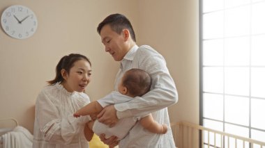 Mutlu ebeveynler, parlak yatak odasında bebeğini sevgiyle bir arada tutarak evde neşeli bir aile ortamı yaratıyor..