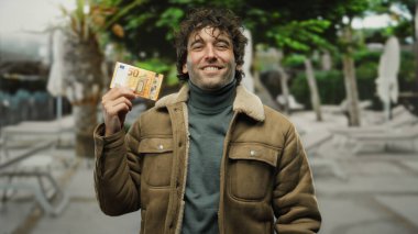 Bir şehir caddesinde elinde 50 avroluk banknotla gülümseyen İspanyol adam, açık hava ve Avrupa para birimi ve gündelik moda kavramını gözler önüne seriyor.