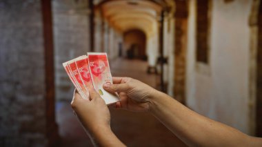 İsrail şekellerini tutan adam, iç mekan ortamında mali yatırım fırsatlarını ön plana çıkarıyor, iş ve para alışverişini yansıtıyor.