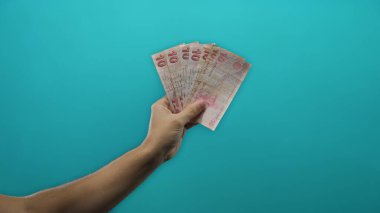 Finansal konsept gösteren mavi arka plan duvarına karşı elinde Türk lirası banknotları tutan adam.