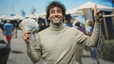 İspanyol adam gülümsüyor, şehrin işlek sokaklarında paralar havada uçuşuyor..