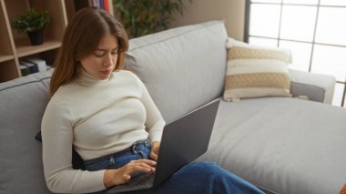 Parlak bir oturma odasında, rahat bir kanepede dizüstü bilgisayar kullanan, modern dekorlarla çevrili, huzurlu bir yaşam tarzı ve teknolojisi olan bir kadın..