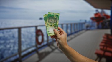 Güney Afrika rand 'ini elinde tutan adam mavi gökyüzünün altındaki sahil limanındaki bir teknede para biriktiriyor..