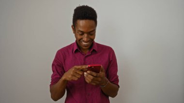 Genç adam gülümserken beyaz arka plan karşısında akıllı telefon kullanıyor neşeli anlar ve teknolojiyle ilgilenen çekici bireyin dijital yaşam tarzını gösteriyor.