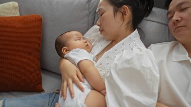 Kadın kanepeye uzanır ve bebeği kucağında tutar. Bu sırada da erkek rahat bir oturma odasında uyur. Huzurlu bir aile anını yakalar..