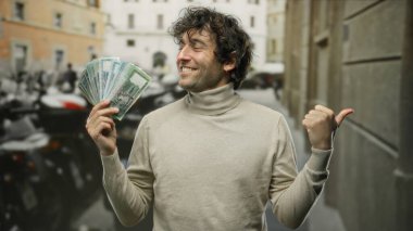 Bangladeşli İspanyol bir adam neşeyle bangladeş taka tutuyor, başparmağıyla işaret ediyor, şehir zemininde şehir atmosferini vurguluyor, açık havada dinamik kentsel yaşam tarzını vurguluyor..