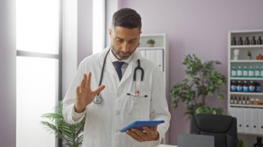 Klinikteki doktor, profesyonel beyaz önlüklü tablet kullanıyor. Hastane ofisinde stetoskop takıyor..