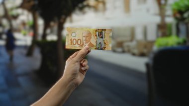 Kentin sokaklarında el ele tutuşan Kanadalı banknotlar, bir adamın varlığı ile şehir manzarasını yakalıyor, halka açık bir ortamda para ve finansal temalar sergiliyor..