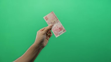 Türk lira banknotunu izole edilmiş yeşil arkaplan duvarı üzerinde tutan adam para birimi temasını gösteriyor.