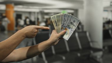 Havaalanı ortamında bir avuç dolarımızı gösteren adam, bulanık bir iç planla çevrili finansal ya da seyahat kavramını resmediyor..