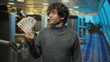 Spor salonunda İngiliz sterlini tutan İspanyol bir adam modern spor merkezinin arka planına karşı para gösteriyor.