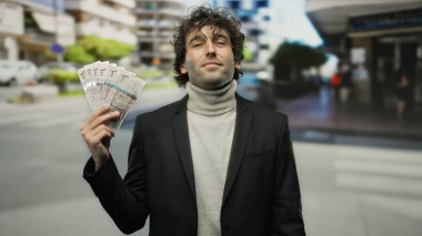 Suudi riyalistleri elinde tutan adam hareketli bir şehir caddesinde duruyor, kentin ortasında şık bir takım elbise giyip İspanyol özelliklerini sergiliyor..