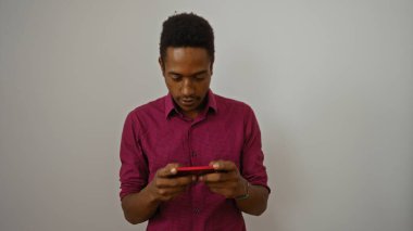 Kırmızı tişörtlü genç adam beyaz arka planda akıllı telefona odaklanmış.