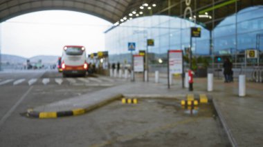 Yağmurlu bir günde, mimari, modern yapı, kıvrımlı çatı ve aydınlatmanın ıslak kaldırıma yansıdığı büyük bir havaalanı terminalinin önündeki otobüs.