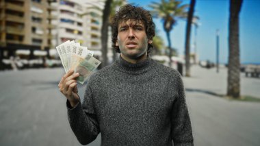 Bir şehir caddesinde elinde Czech Koruna banknotları tutan bir adam, açık şehir arka planı ve günlük kıyafetlerle finansal temayı tasvir ederek, para değişimi veya ekonomik konsept öneriyor.