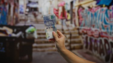 Kentsel caddede el ele tutuşan Güney Afrika rand banknotu, graffiti arka planda para, finans ve açık şehir hayatı sergiliyor..