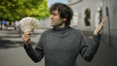 Bir şehir caddesinde elinde Rus rublesi tutan İspanyol bir adam bulanık bir geçmişi olduğunu belirterek şehir yaşamını ve ekonomik temaları vurguluyor..