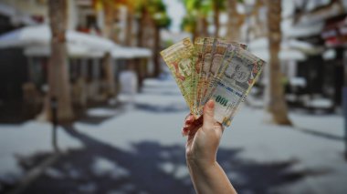 Güneşli bir şehir sokağında taban tutan Perulu kadın, hareketli bir şehir ortamında iş ve para alışverişini ön plana çıkarıyor..