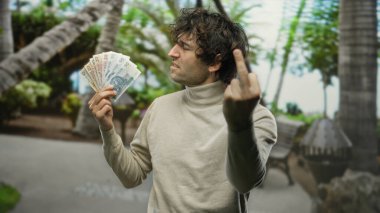 Parkta parktaki İspanyol adam elinde kızgın bir ifade ve orta parmak hareketiyle, bulanık doğal yeşillik ile çevrili Polonyalı zloti banknotları tutuyor..