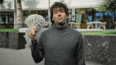 Amerika Birleşik Devletleri dolarlarını elinde tutan İspanyol bir adam şehir caddesinde, arka planda modern kentsel fon ile açık havada para sergiliyor..