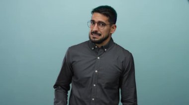 Mavi arka planda küçük parmakları olan Latin kökenli genç adam belirsizlik ve ifade taşıyor.