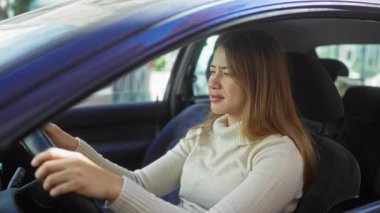 Kentsel caddede süveter giyen bir kadın gülerek gülerek araba kullanıyor.